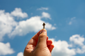 Hand hält Kreuz in den Himmel